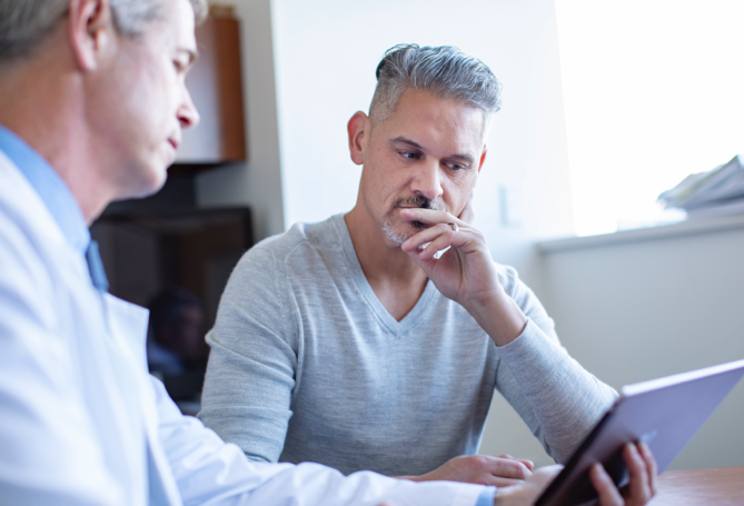 Middle-aged man with doctor reading computer screen.